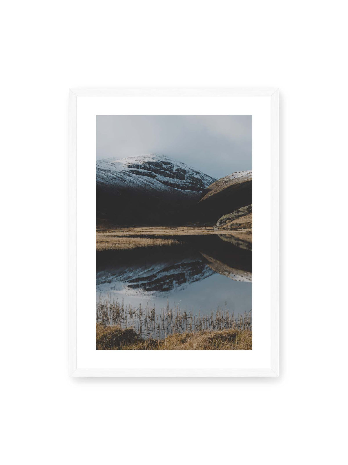 50x70 cm, weißer Galerie-Rand, weißer Rahmen – Schneebedeckte Berghänge spiegeln sich in einem stillen Gewässer, umgeben von hellen Gräsern und Schilf.