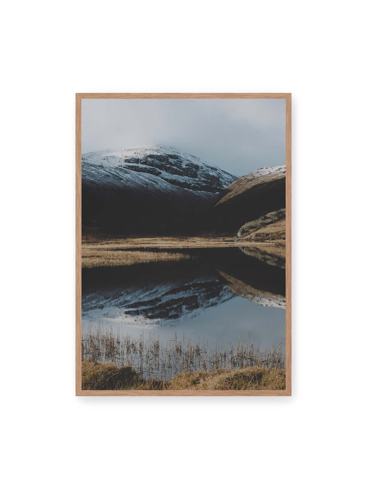 70x100 cm, Eichenrahmen – Schneebedeckte Berghänge spiegeln sich in einem stillen Gewässer, umgeben von hellen Gräsern und Schilf.