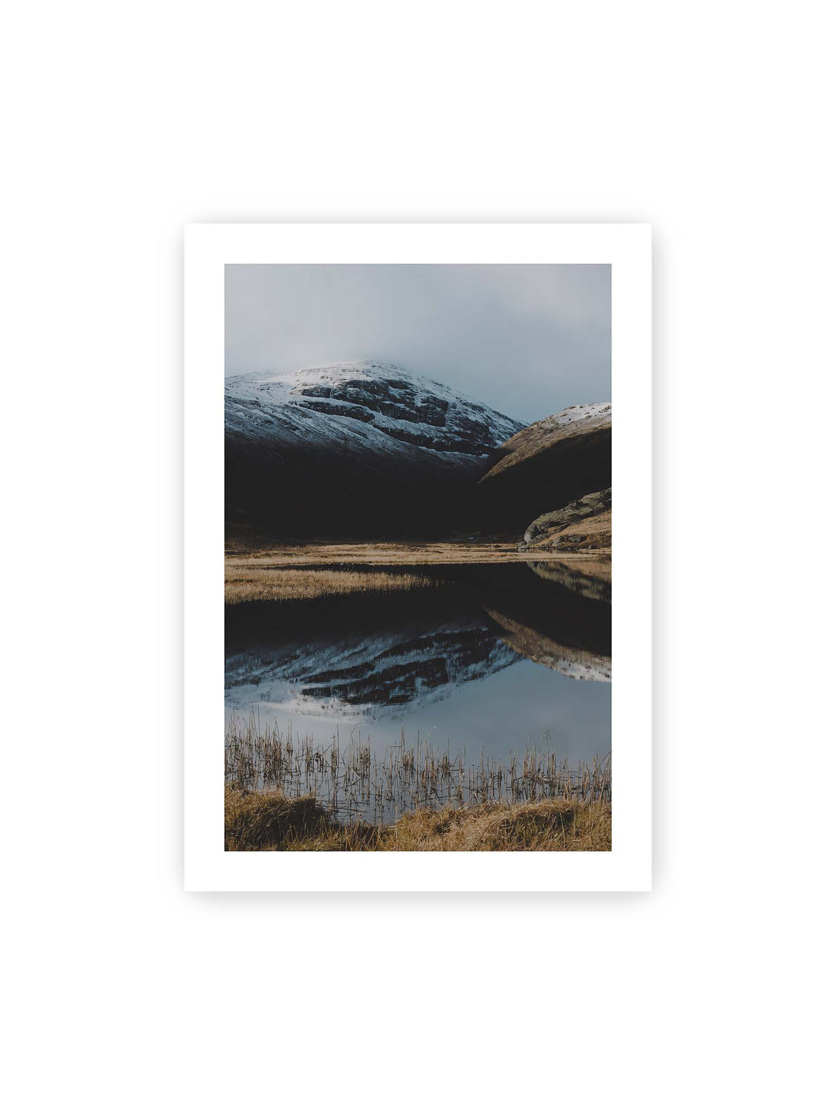 70x100 cm, weißer Galerie-Rand – Schneebedeckte Berghänge spiegeln sich in einem stillen Gewässer, umgeben von hellen Gräsern und Schilf.