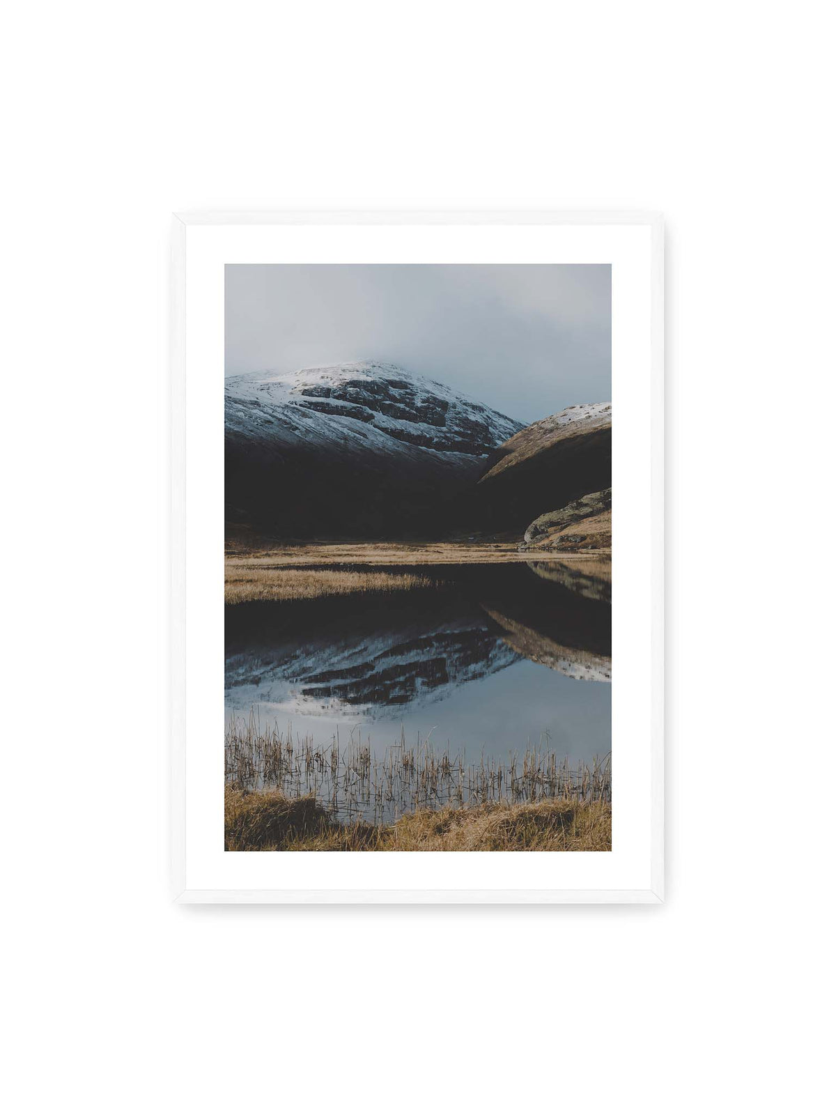 70x100 cm, weißer Galerie-Rand, weißer Rahmen – Schneebedeckte Berghänge spiegeln sich in einem stillen Gewässer, umgeben von hellen Gräsern und Schilf.