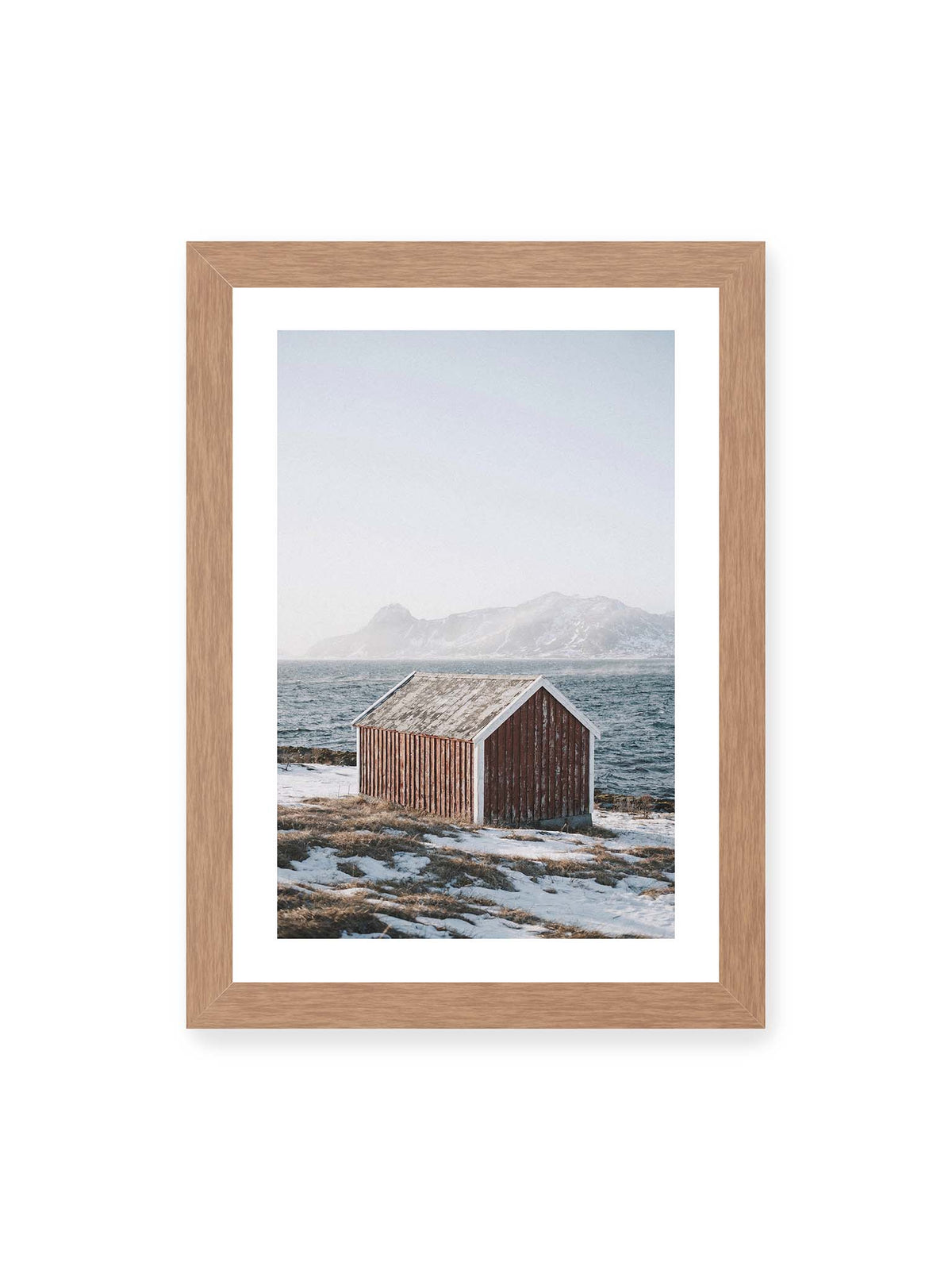 21x30 cm, weißer Galerie-Rand, Eichenrahmen – Verwitterte rote Holzhütte an einer verschneiten Küste mit dunklem Wasser und felsigen Bergen im Hintergrund.