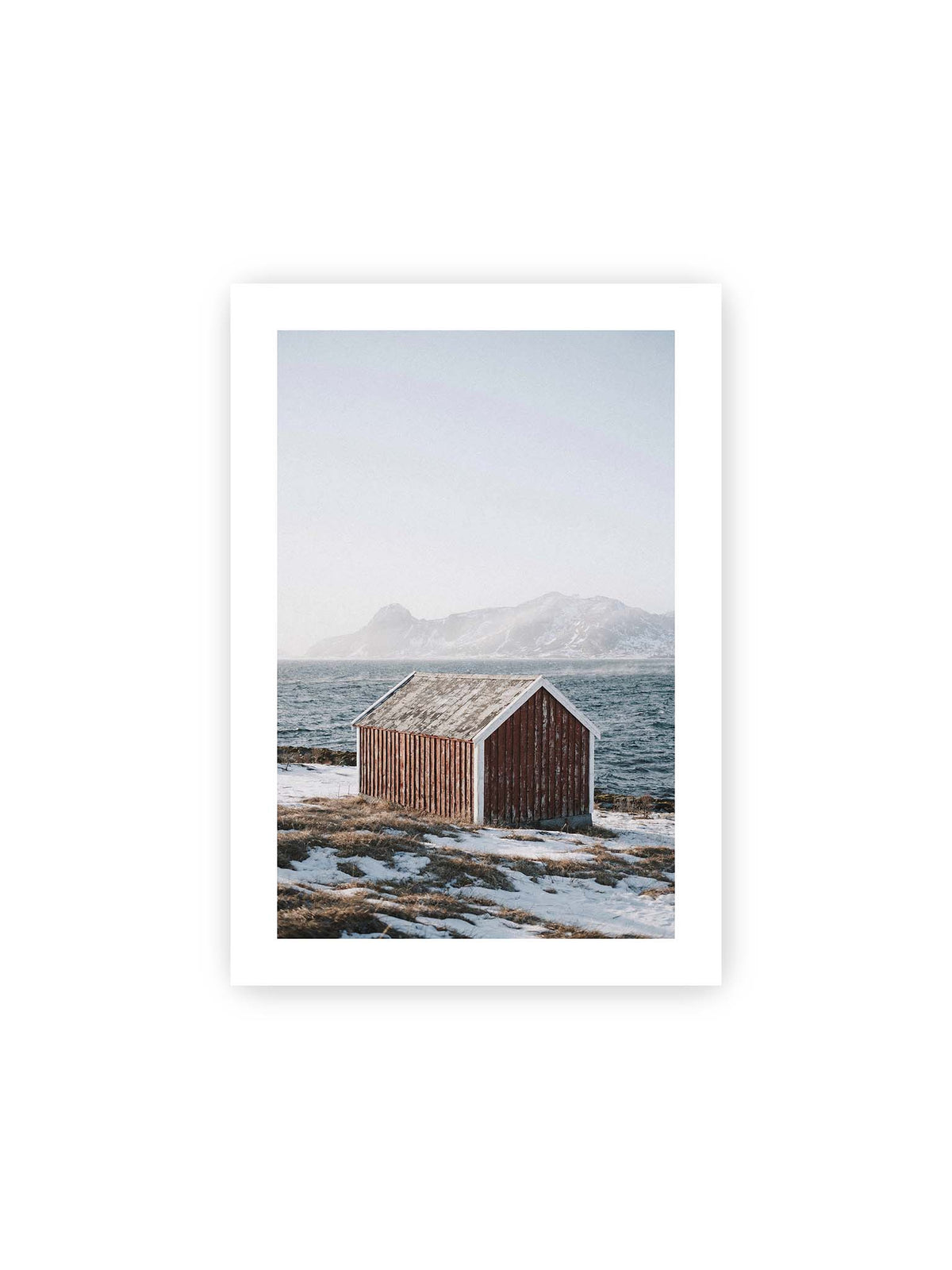 21x30 cm, weißer Galerie-Rand – Verwitterte rote Holzhütte an einer verschneiten Küste mit dunklem Wasser und felsigen Bergen im Hintergrund.