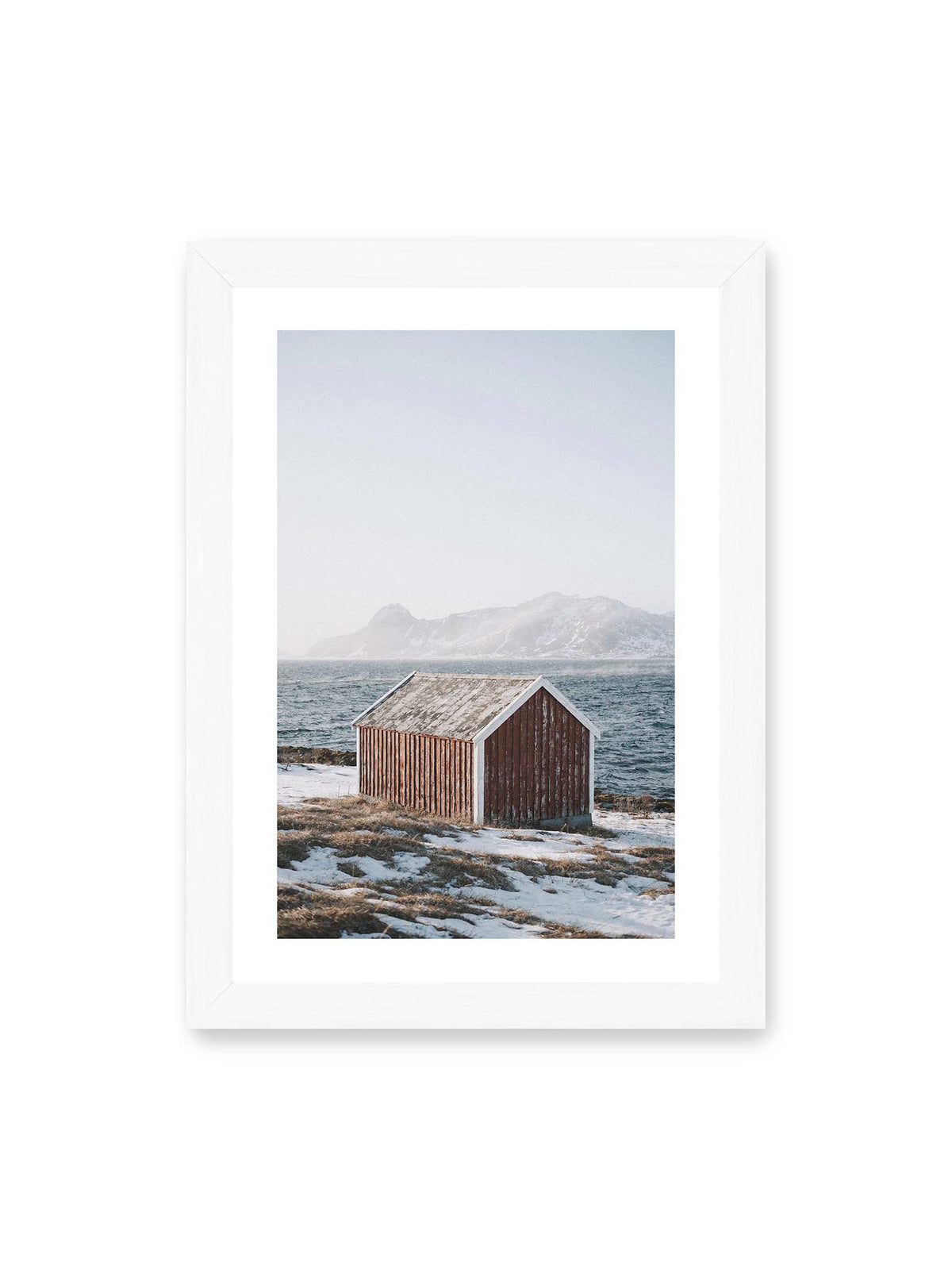 21x30 cm, weißer Galerie-Rand, weißer Rahmen – Verwitterte rote Holzhütte an einer verschneiten Küste mit dunklem Wasser und felsigen Bergen im Hintergrund.
