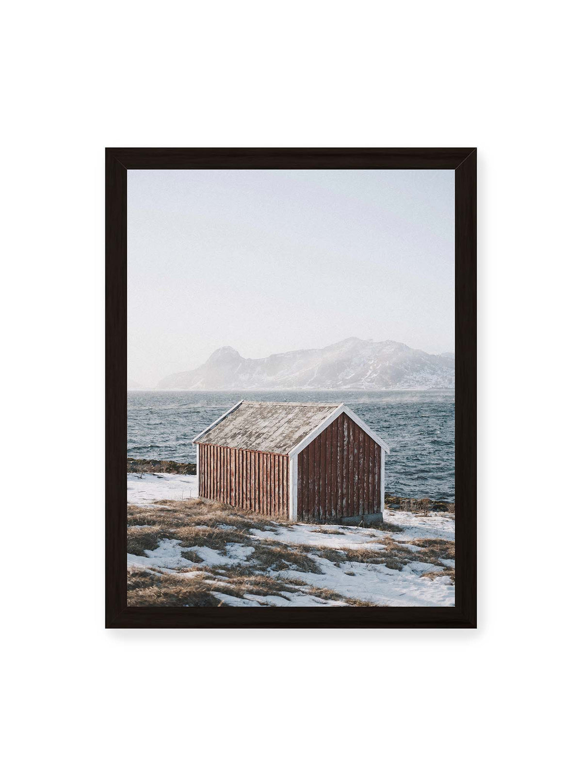 30x40 cm, schwarzer Rahmen – Verwitterte rote Holzhütte an einer verschneiten Küste mit dunklem Wasser und felsigen Bergen im Hintergrund.