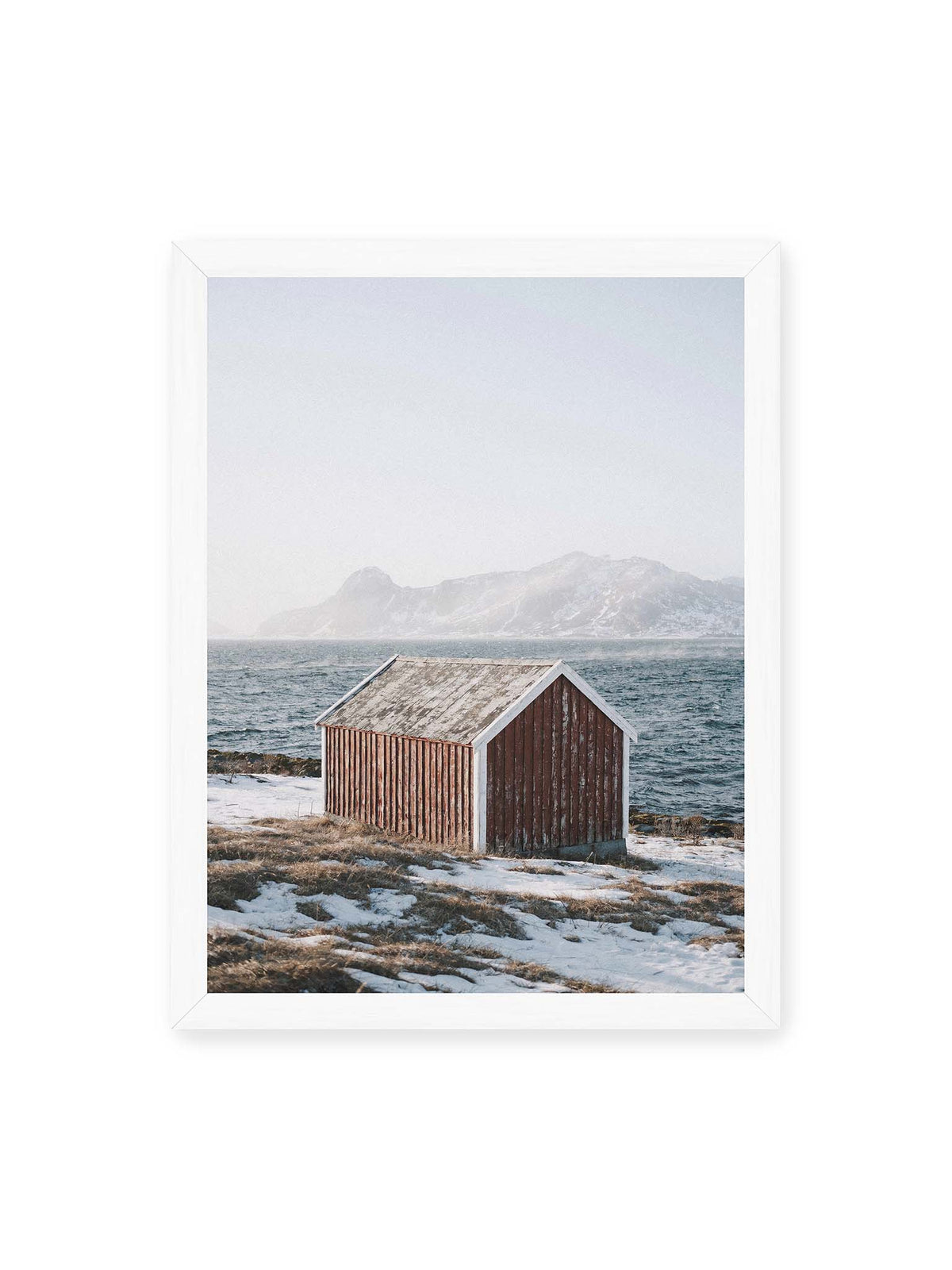 30x40 cm, weißer Rahmen – Verwitterte rote Holzhütte an einer verschneiten Küste mit dunklem Wasser und felsigen Bergen im Hintergrund.