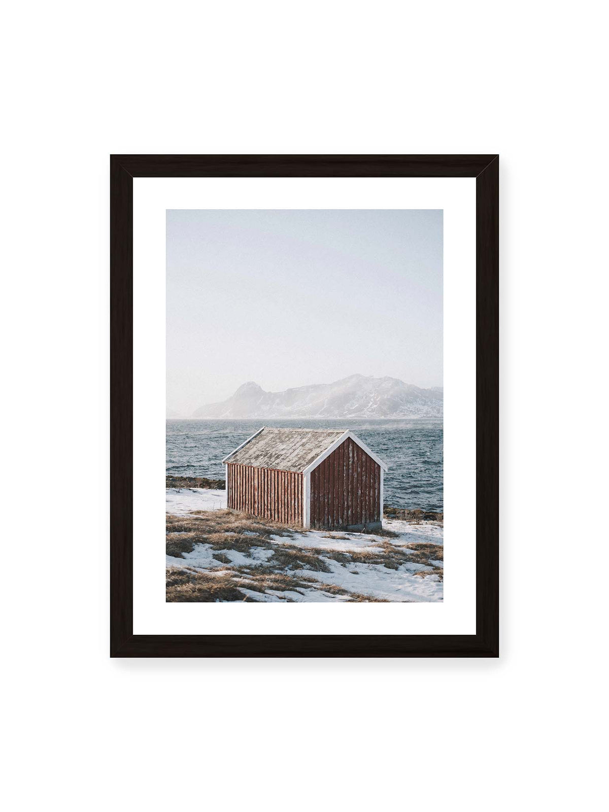 30x40 cm, weißer Galerie-Rand, schwarzer Rahmen – Verwitterte rote Holzhütte an einer verschneiten Küste mit dunklem Wasser und felsigen Bergen im Hintergrund.