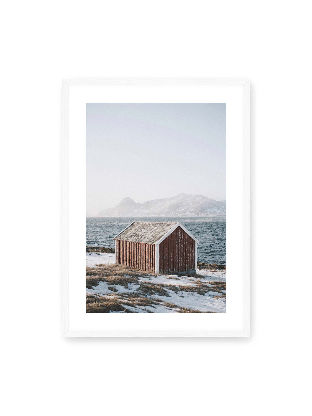 50x70 cm, weißer Galerie-Rand, weißer Rahmen – Verwitterte rote Holzhütte an einer verschneiten Küste mit dunklem Wasser und felsigen Bergen im Hintergrund.