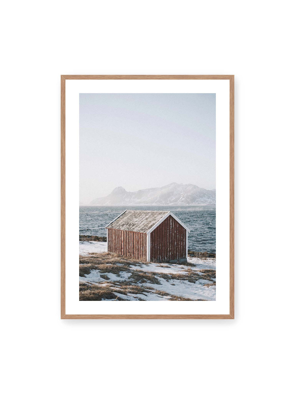 70x100 cm, weißer Galerie-Rand, Eichenrahmen – Verwitterte rote Holzhütte an einer verschneiten Küste mit dunklem Wasser und felsigen Bergen im Hintergrund.