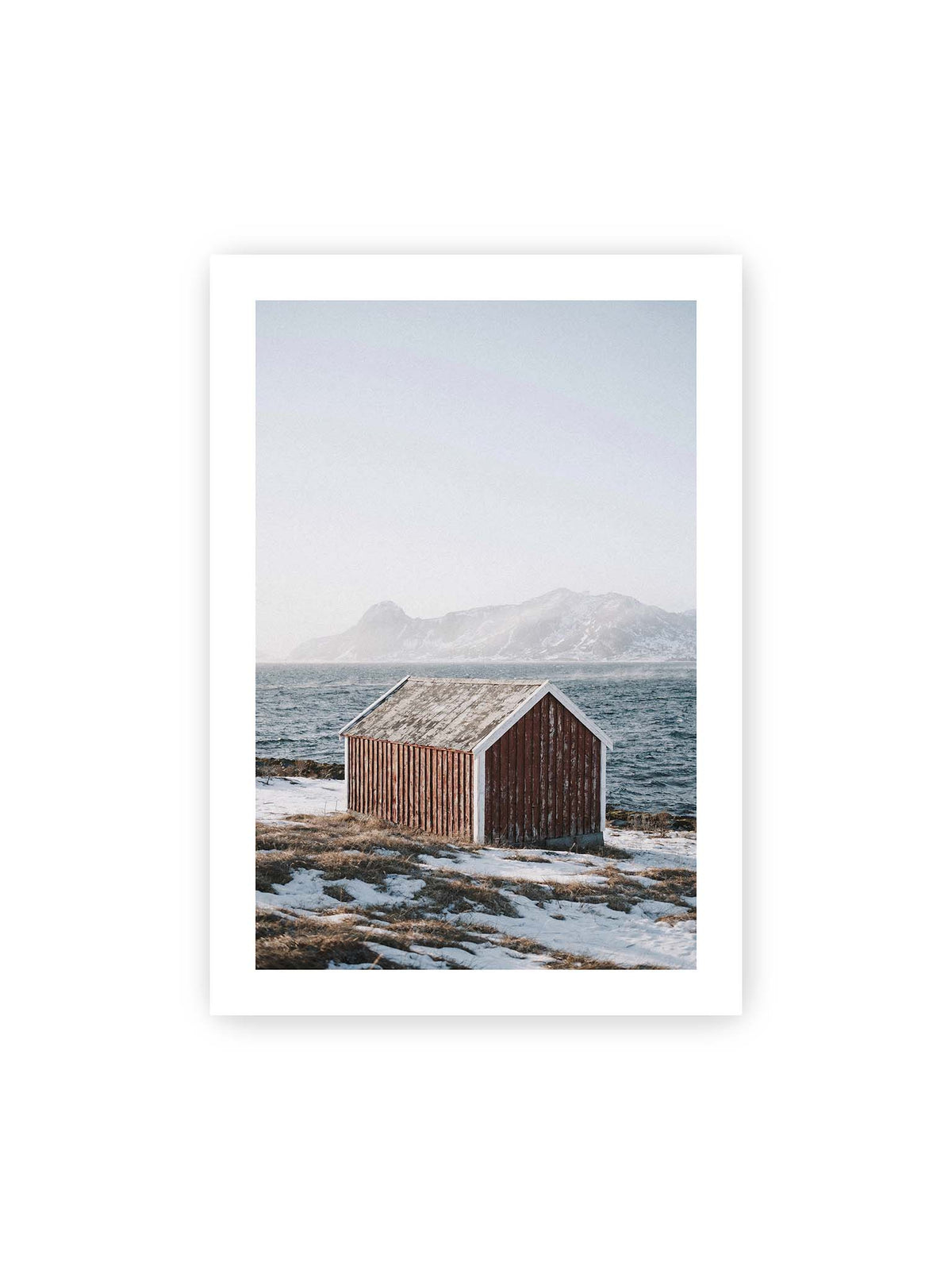 70x100 cm, weißer Galerie-Rand – Verwitterte rote Holzhütte an einer verschneiten Küste mit dunklem Wasser und felsigen Bergen im Hintergrund.