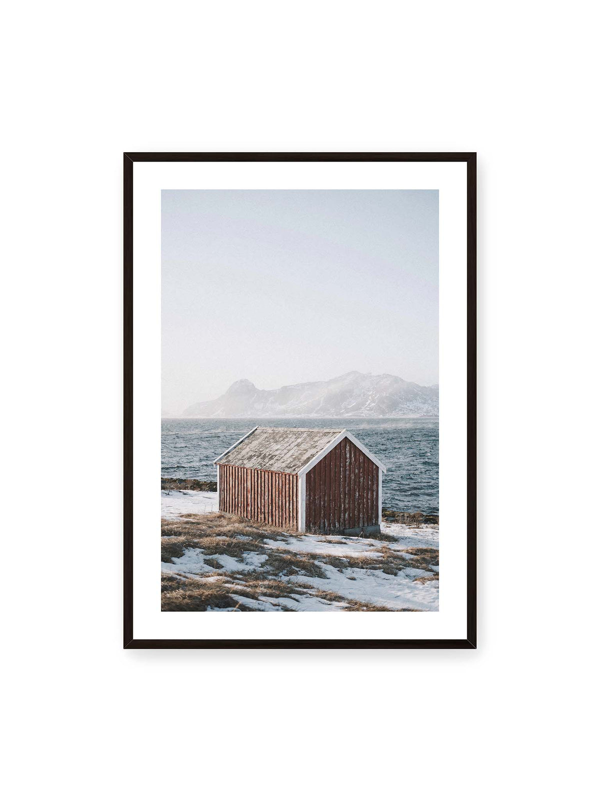 70x100 cm, weißer Galerie-Rand, schwarzer Rahmen – Verwitterte rote Holzhütte an einer verschneiten Küste mit dunklem Wasser und felsigen Bergen im Hintergrund.