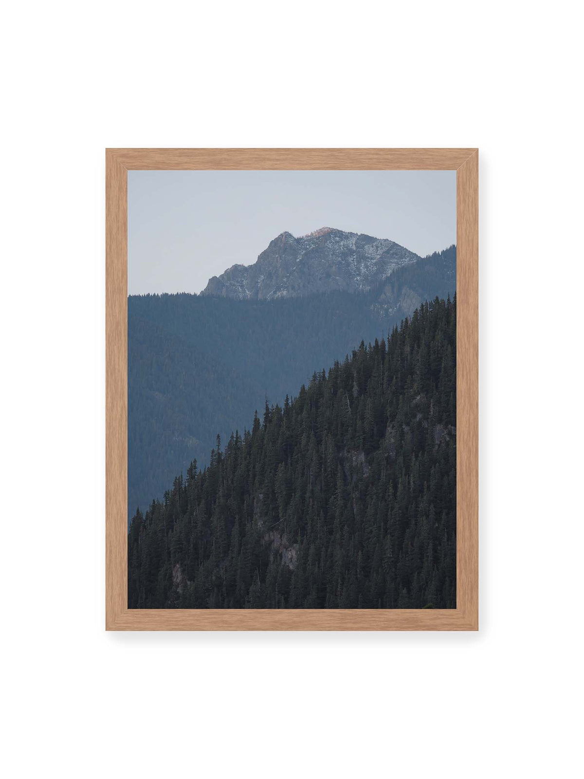 30x40 cm, Eichenrahmen – Bewaldete Berghänge staffeln sich vor einem felsigen Gipfel mit einzelnen Schneeflächen und blaugrauem Himmel.