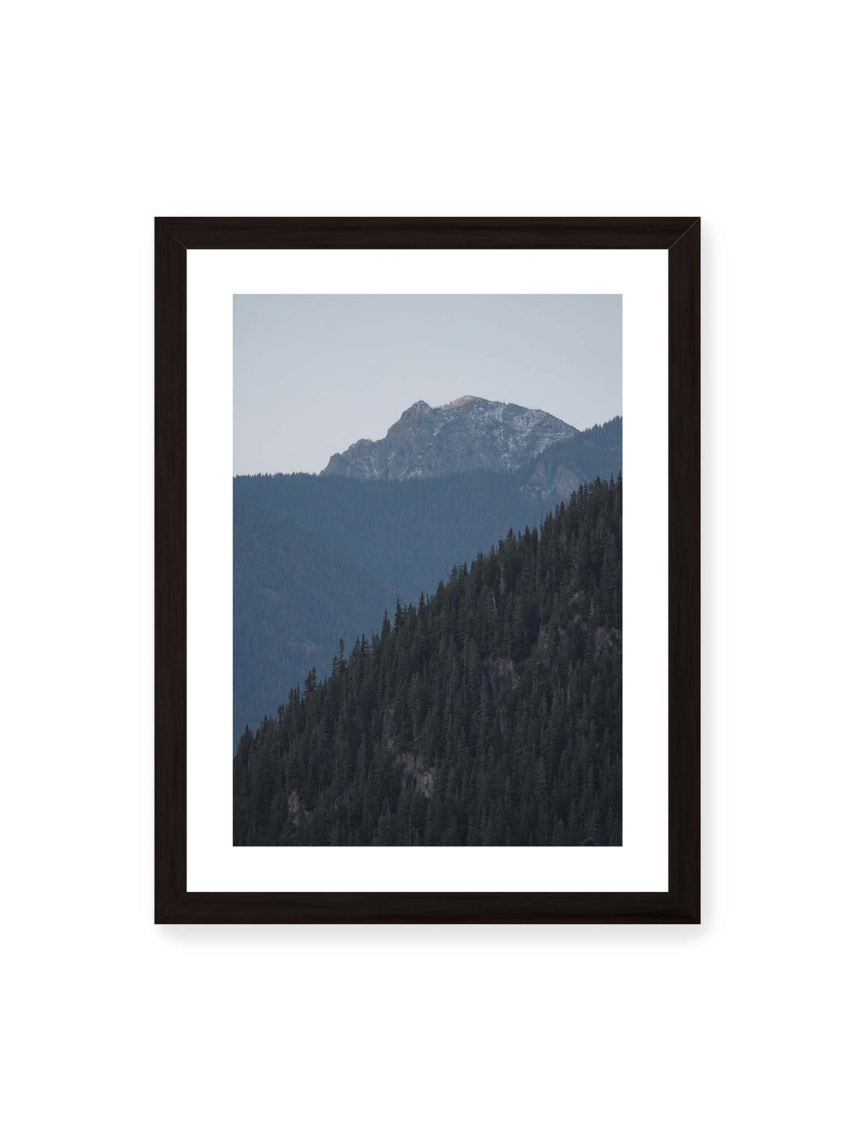 30x40 cm, weißer Galerie-Rand, schwarzer Rahmen – Bewaldete Berghänge staffeln sich vor einem felsigen Gipfel mit einzelnen Schneeflächen und blaugrauem Himmel.