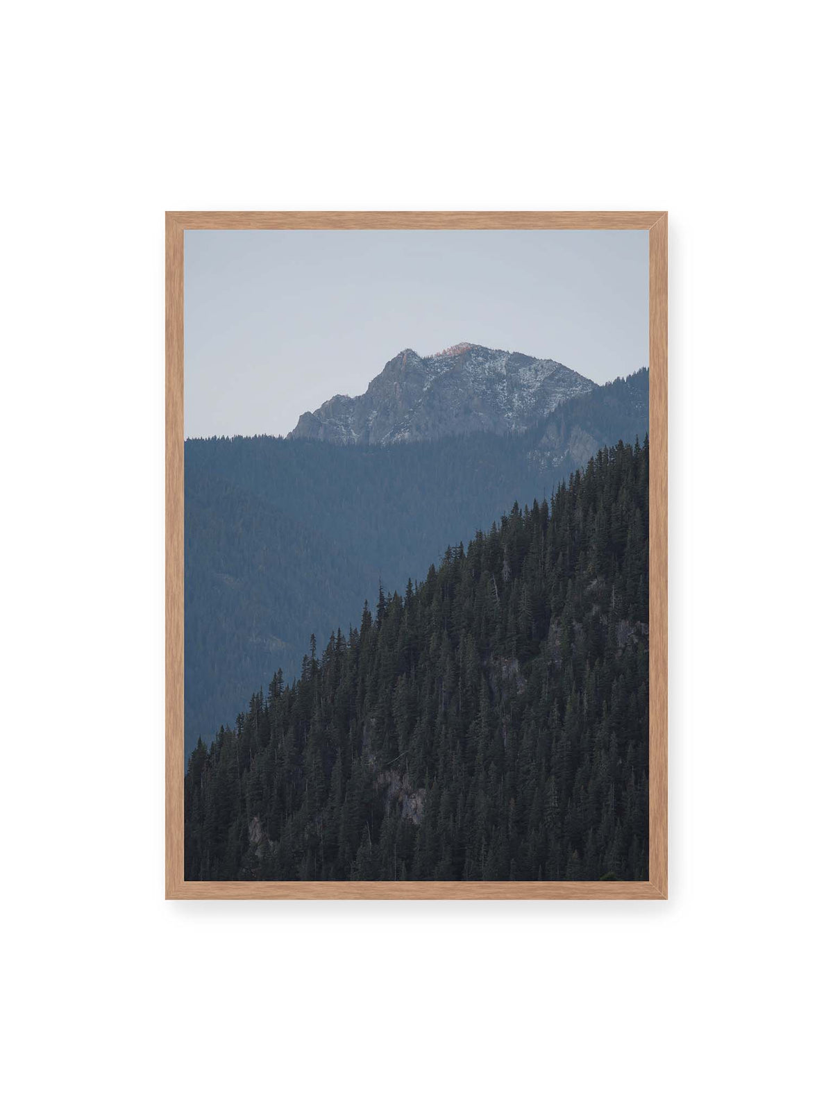 50x70 cm, Eichenrahmen – Bewaldete Berghänge staffeln sich vor einem felsigen Gipfel mit einzelnen Schneeflächen und blaugrauem Himmel.