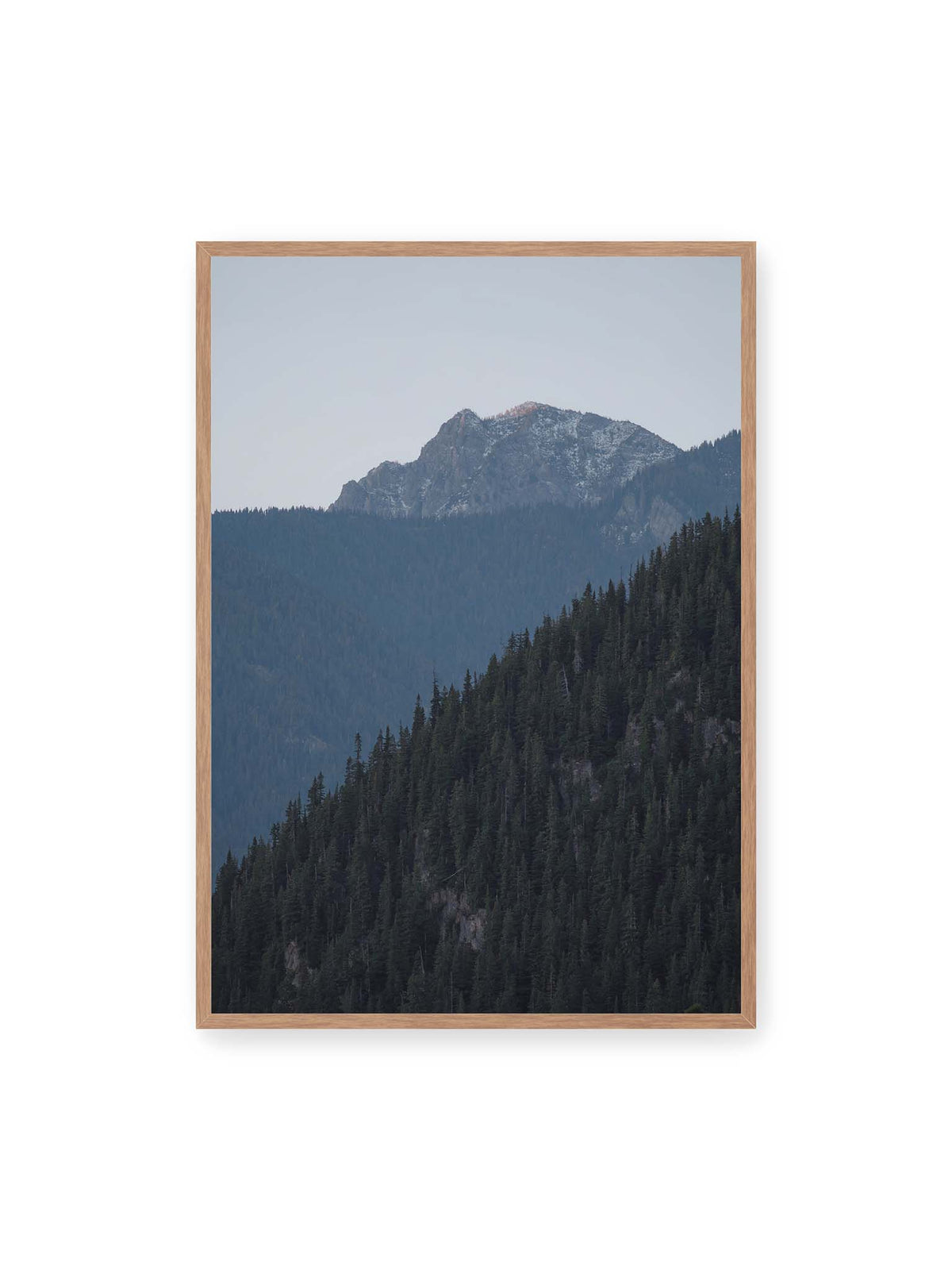 70x100 cm, Eichenrahmen – Bewaldete Berghänge staffeln sich vor einem felsigen Gipfel mit einzelnen Schneeflächen und blaugrauem Himmel.