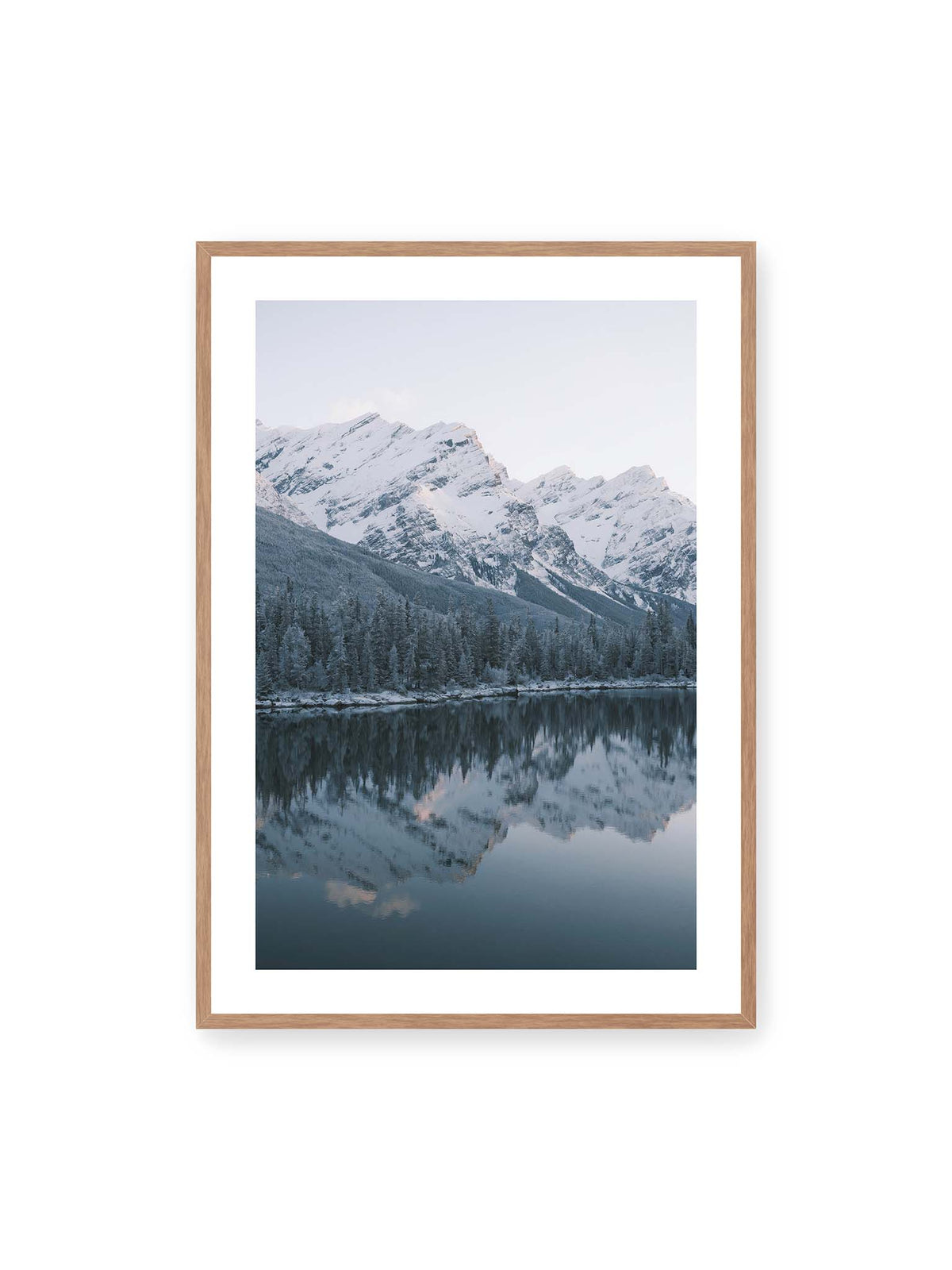 70x100 cm, weißer Galerie-Rand, Eichenrahmen – Verschneite Berggipfel und dichter Nadelwald spiegeln sich in einem ruhigen, blaugrauen See.