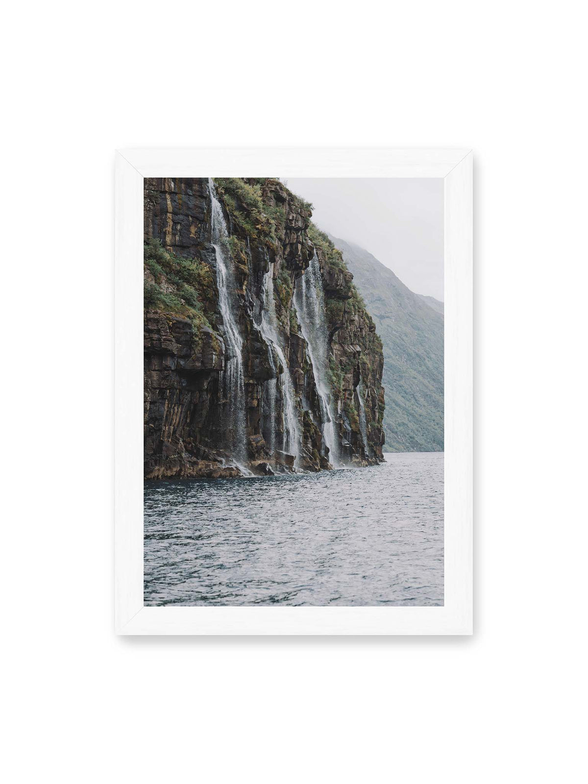 21x30 cm, weißer Rahmen – Mehrere Wasserfälle stürzen über eine dunkle, bewachsene Felswand direkt in eine weite Wasserfläche.