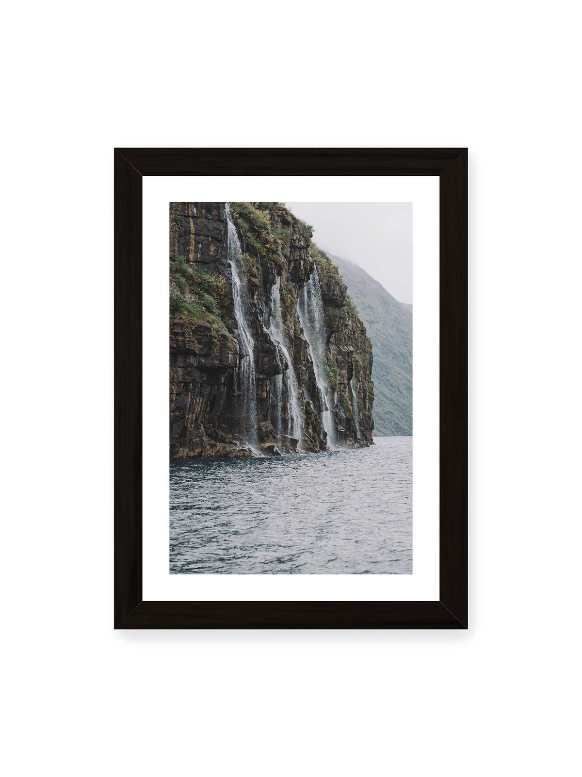 21x30 cm, weißer Galerie-Rand, schwarzer Rahmen – Mehrere Wasserfälle stürzen über eine dunkle, bewachsene Felswand direkt in eine weite Wasserfläche.