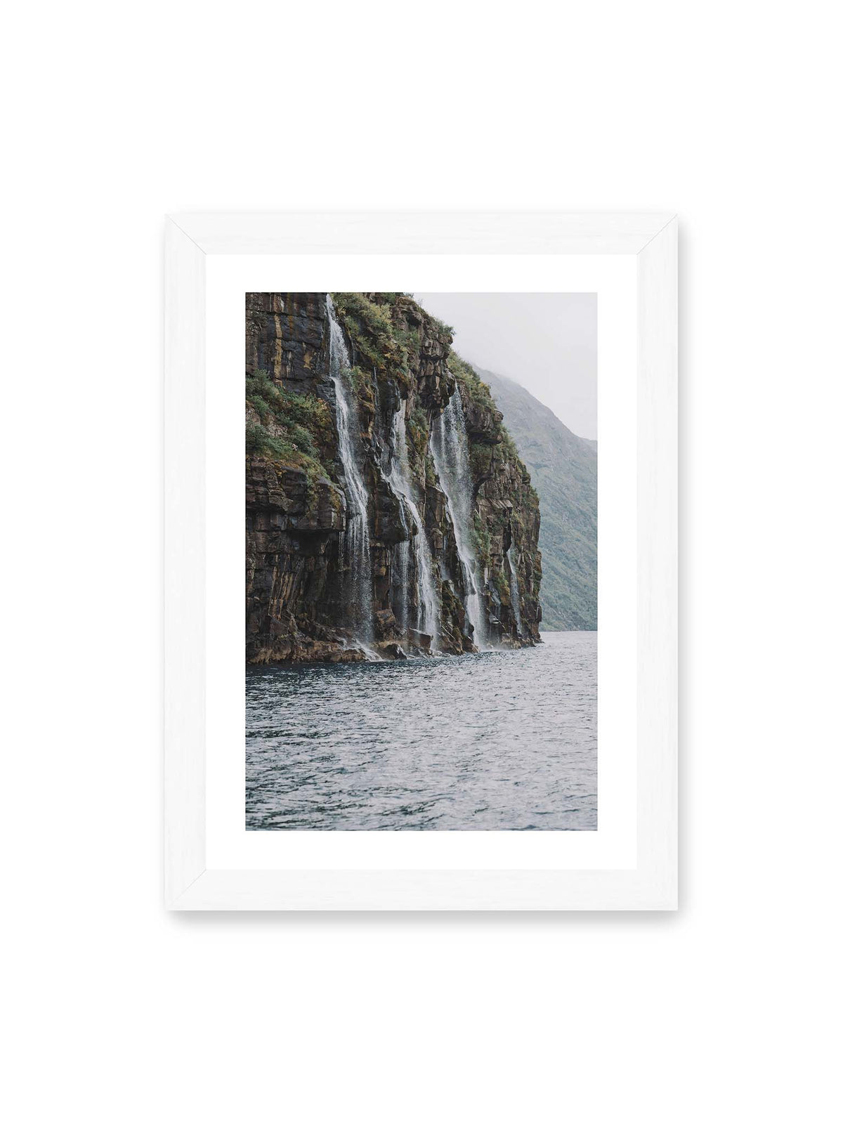 21x30 cm, weißer Galerie-Rand, weißer Rahmen – Mehrere Wasserfälle stürzen über eine dunkle, bewachsene Felswand direkt in eine weite Wasserfläche.