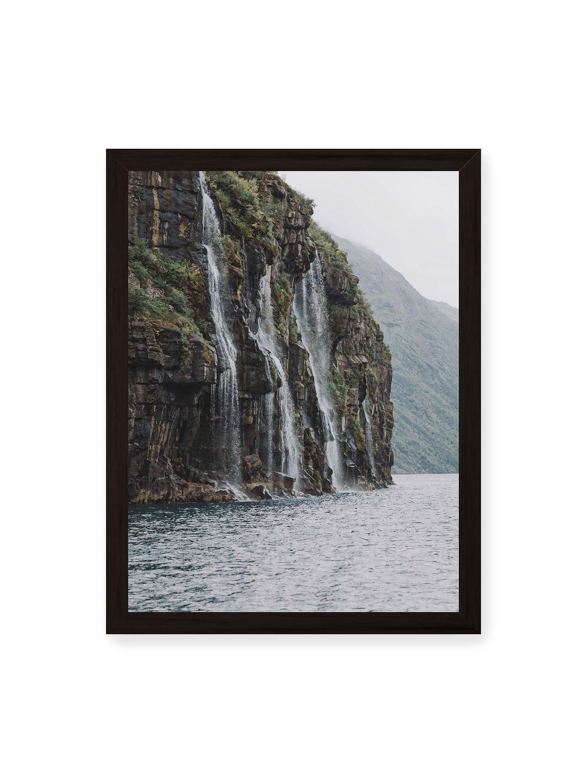 30x40 cm, schwarzer Rahmen – Mehrere Wasserfälle stürzen über eine dunkle, bewachsene Felswand direkt in eine weite Wasserfläche.