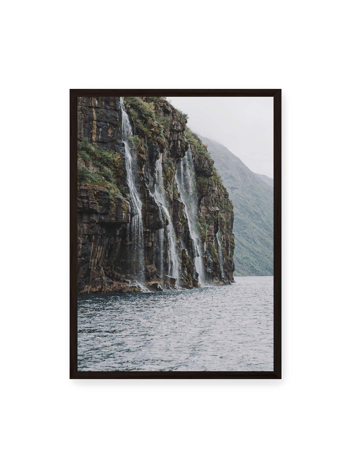 50x70 cm, schwarzer Rahmen – Mehrere Wasserfälle stürzen über eine dunkle, bewachsene Felswand direkt in eine weite Wasserfläche.