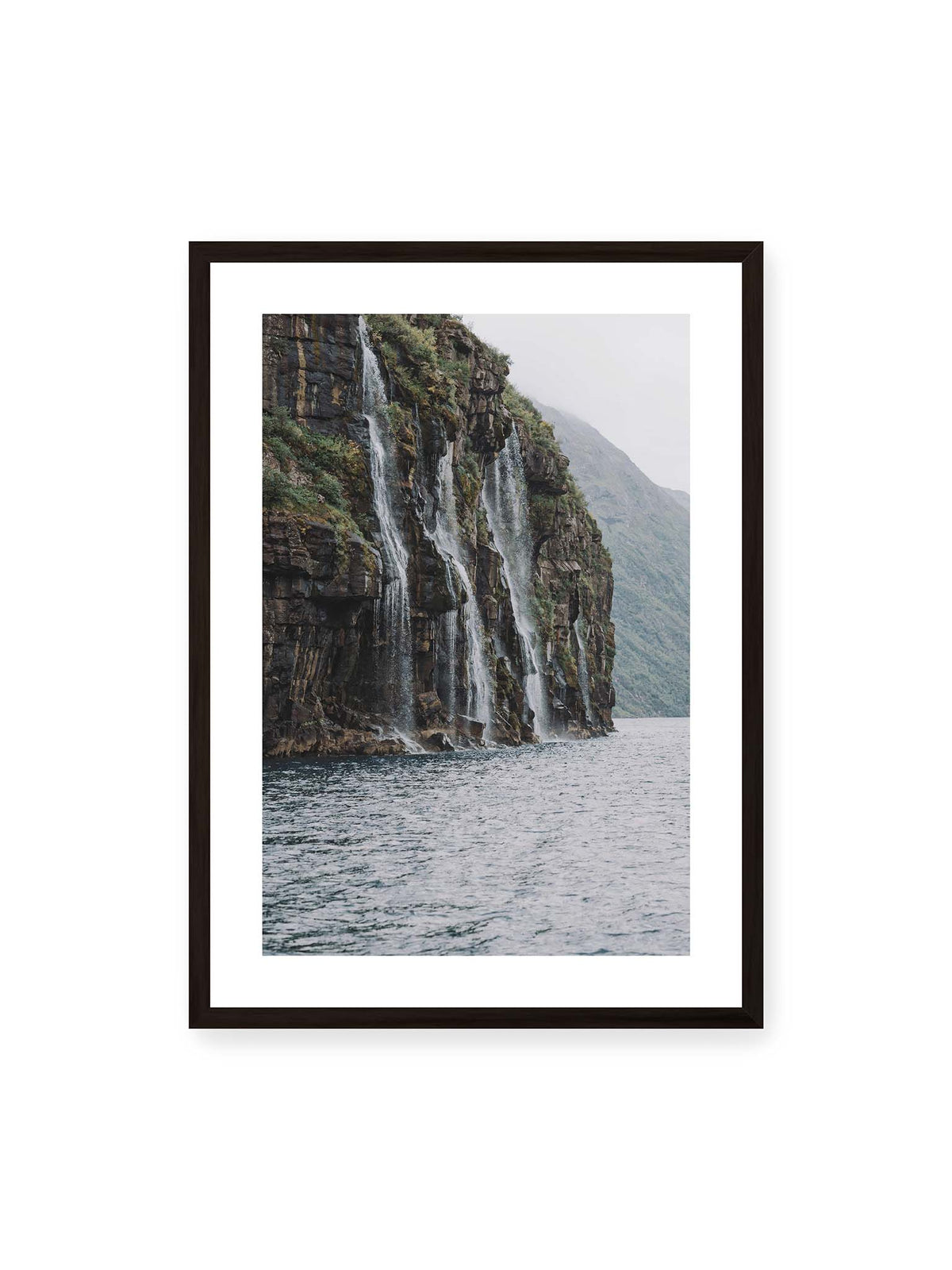 50x70 cm, weißer Galerie-Rand, schwarzer Rahmen – Mehrere Wasserfälle stürzen über eine dunkle, bewachsene Felswand direkt in eine weite Wasserfläche.
