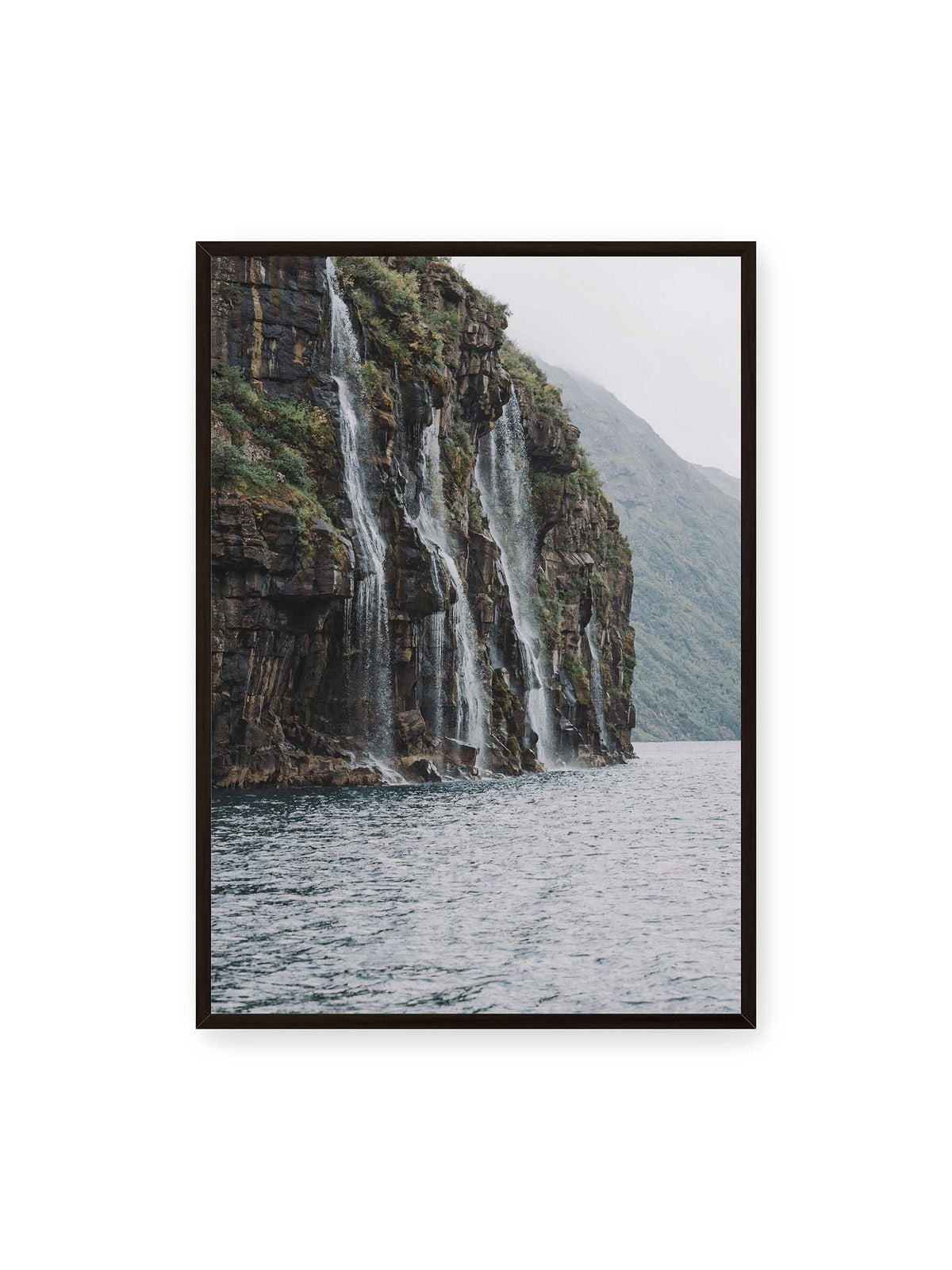70x100 cm, schwarzer Rahmen – Mehrere Wasserfälle stürzen über eine dunkle, bewachsene Felswand direkt in eine weite Wasserfläche.