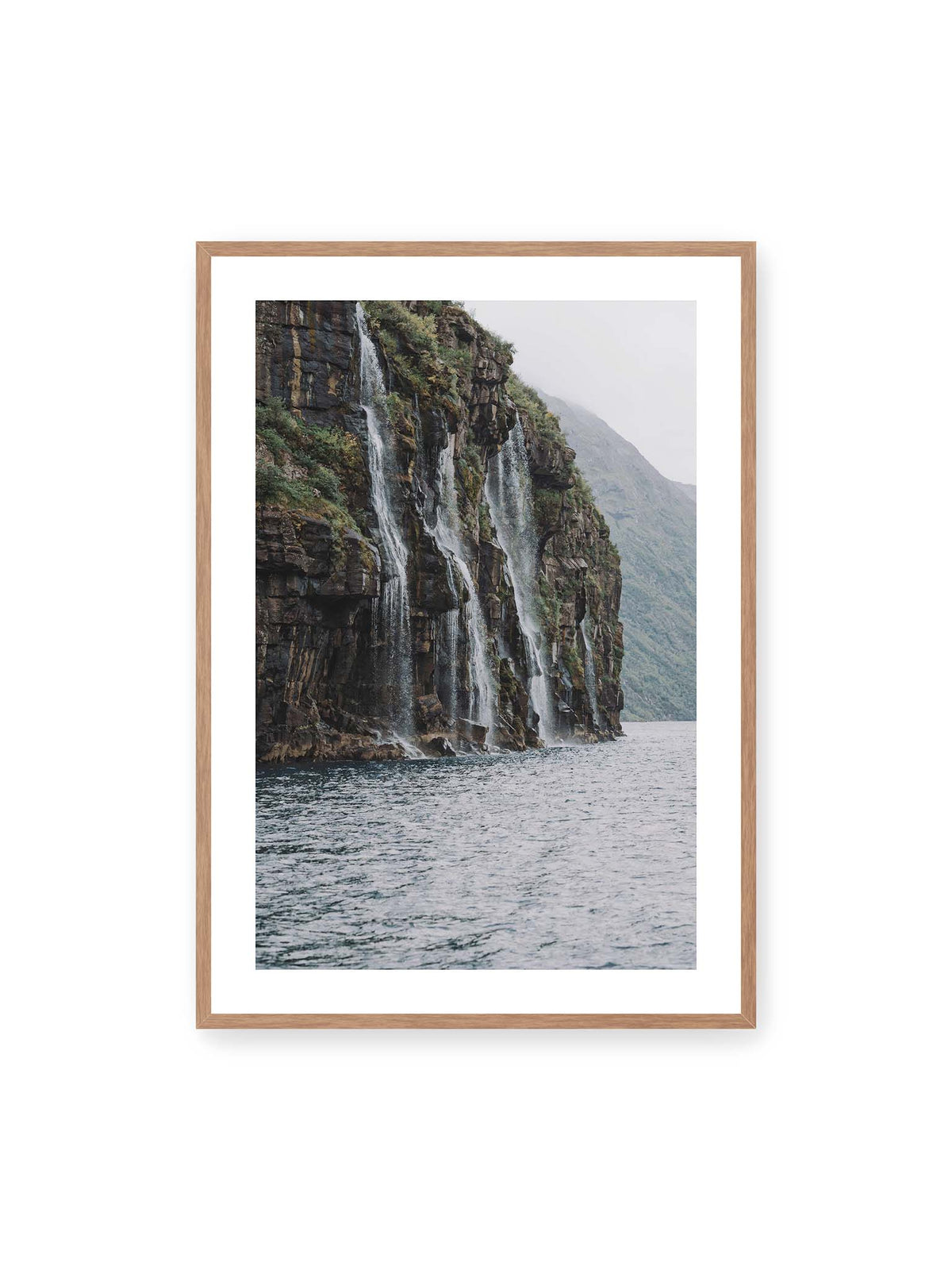 70x100 cm, weißer Galerie-Rand, Eichenrahmen – Mehrere Wasserfälle stürzen über eine dunkle, bewachsene Felswand direkt in eine weite Wasserfläche.