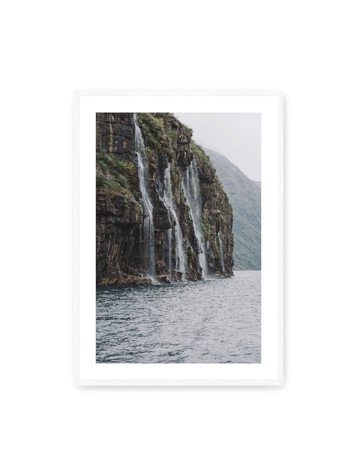 70x100 cm, weißer Galerie-Rand, weißer Rahmen – Mehrere Wasserfälle stürzen über eine dunkle, bewachsene Felswand direkt in eine weite Wasserfläche.