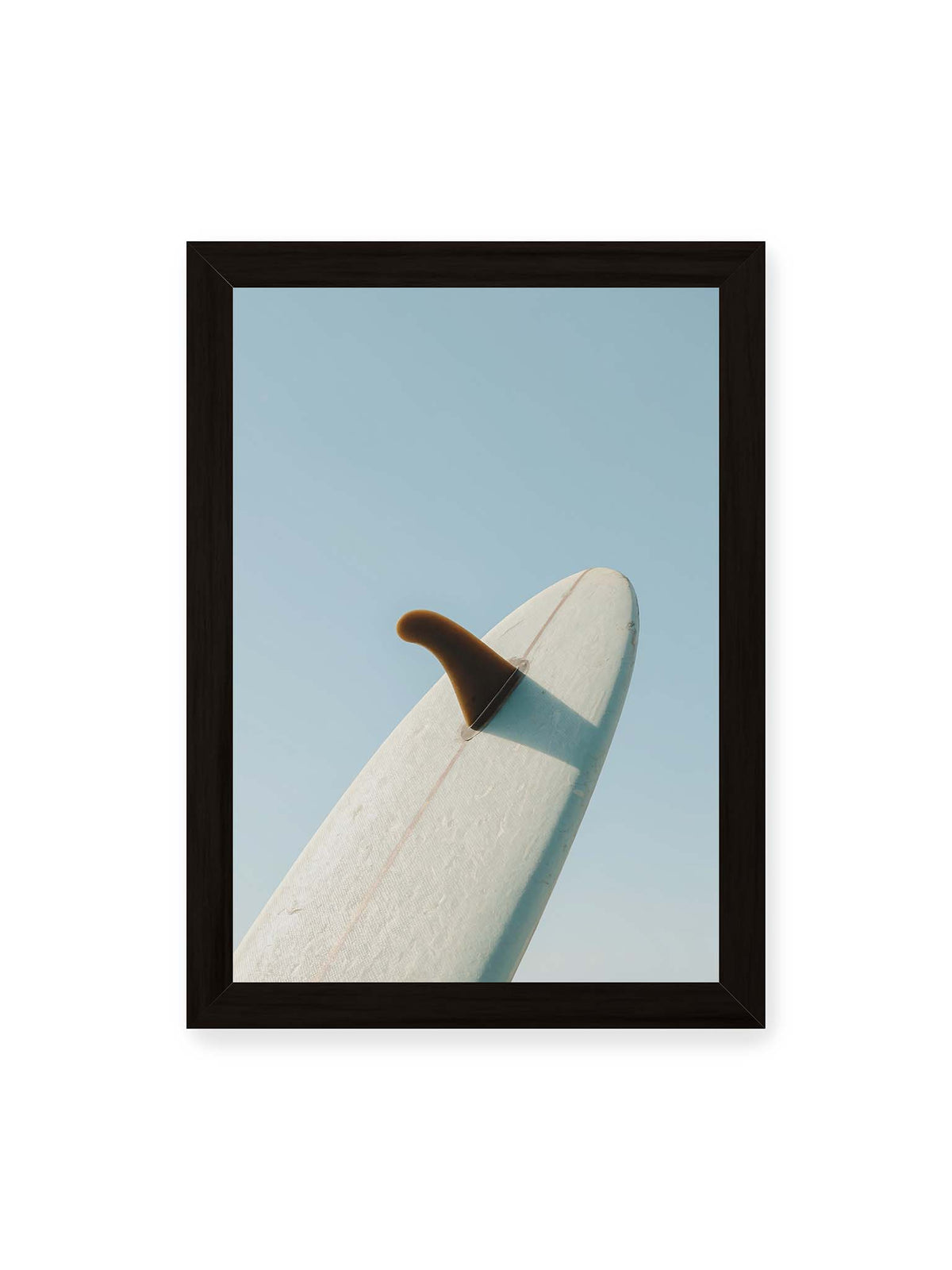 21x30 cm, schwarzer Rahmen – Helles Surfbrett mit dunkler Finne und markantem Schatten ragt diagonal vor einen klaren blauen Himmel.