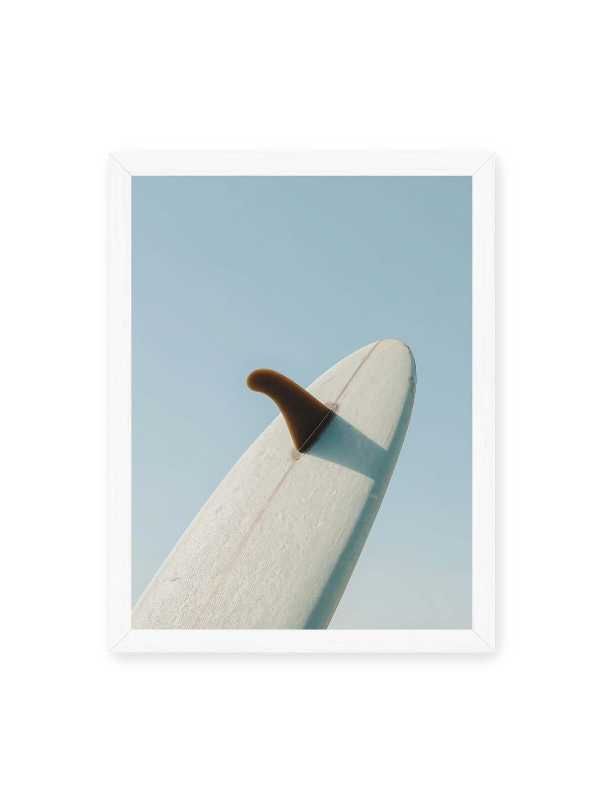 30x40 cm, weißer Rahmen – Helles Surfbrett mit dunkler Finne und markantem Schatten ragt diagonal vor einen klaren blauen Himmel.