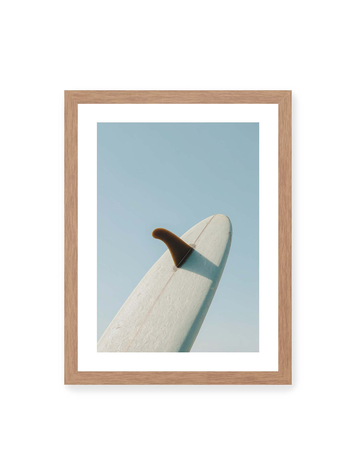 30x40 cm, weißer Galerie-Rand, Eichenrahmen – Helles Surfbrett mit dunkler Finne und markantem Schatten ragt diagonal vor einen klaren blauen Himmel.