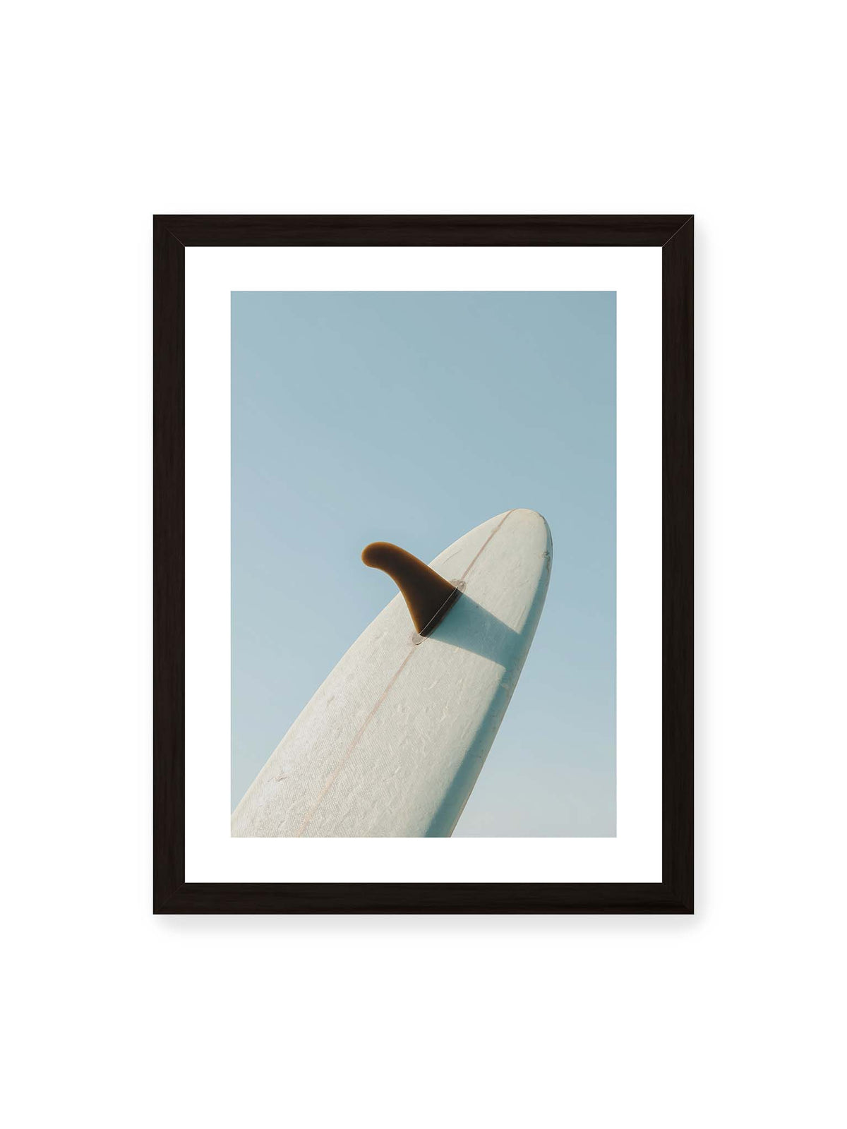 30x40 cm, weißer Galerie-Rand, schwarzer Rahmen – Helles Surfbrett mit dunkler Finne und markantem Schatten ragt diagonal vor einen klaren blauen Himmel.