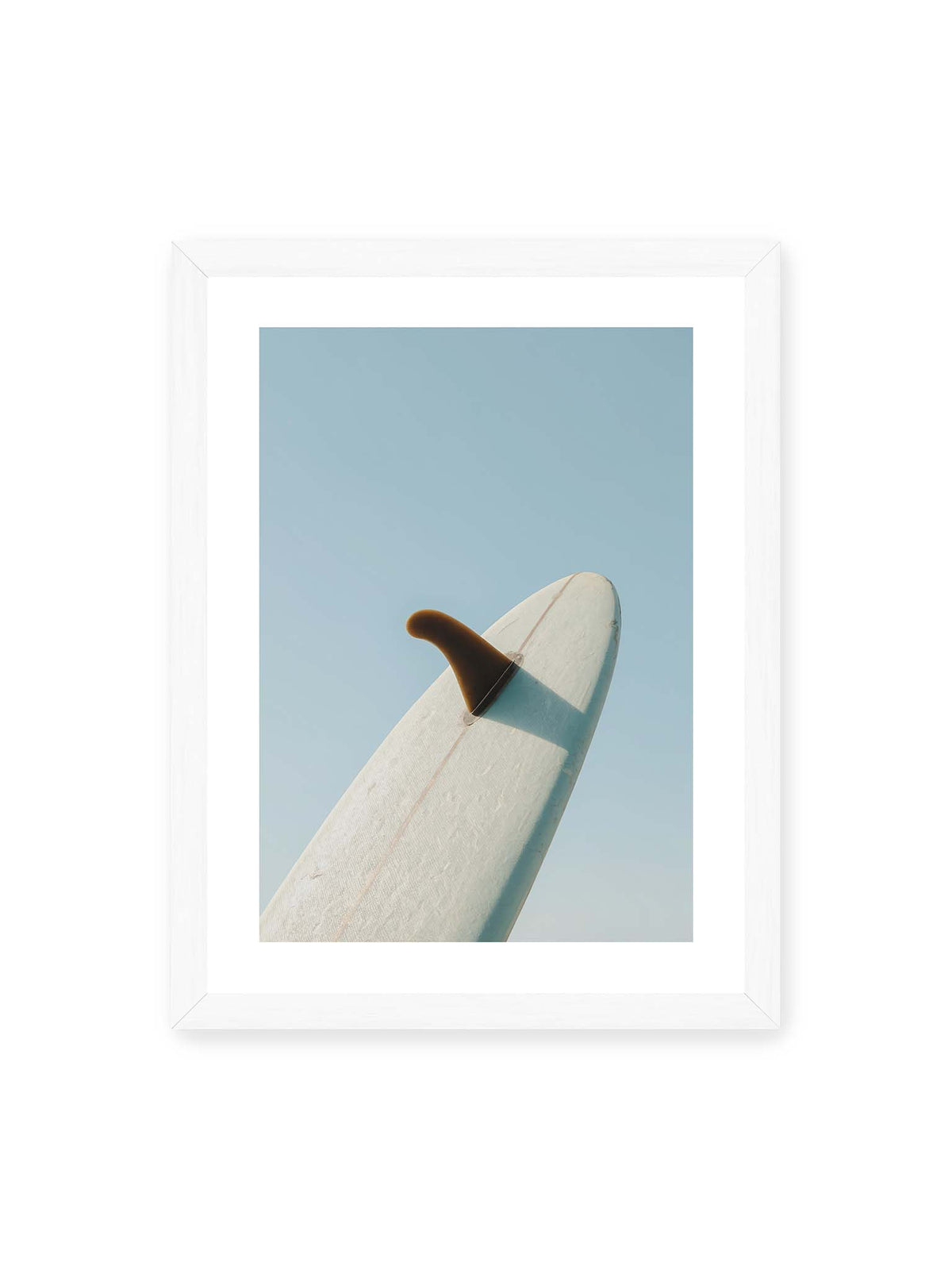 30x40 cm, weißer Galerie-Rand, weißer Rahmen – Helles Surfbrett mit dunkler Finne und markantem Schatten ragt diagonal vor einen klaren blauen Himmel.