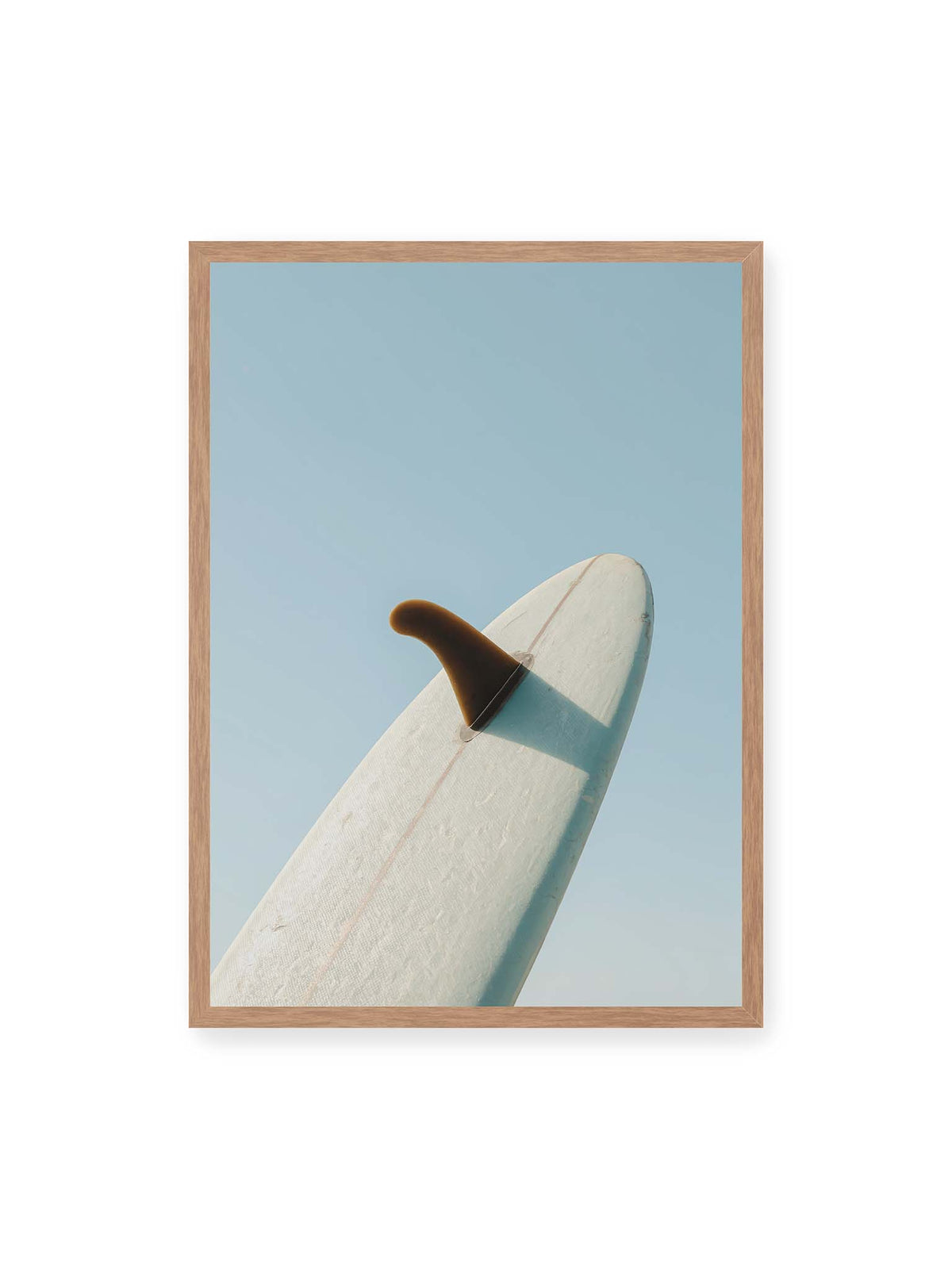 50x70 cm, Eichenrahmen – Helles Surfbrett mit dunkler Finne und markantem Schatten ragt diagonal vor einen klaren blauen Himmel.