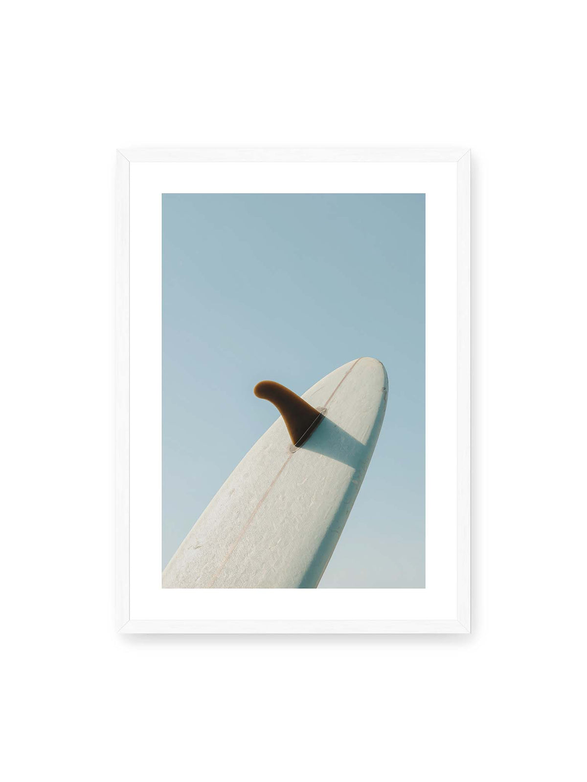 50x70 cm, weißer Galerie-Rand, weißer Rahmen – Helles Surfbrett mit dunkler Finne und markantem Schatten ragt diagonal vor einen klaren blauen Himmel.