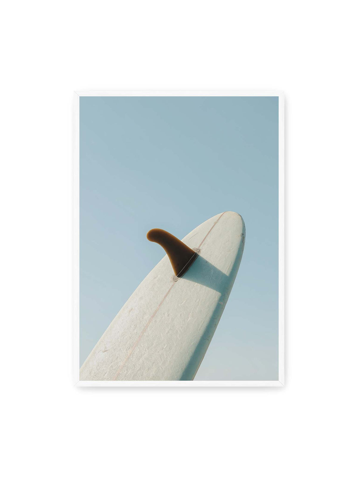 70x100 cm, weißer Rahmen – Helles Surfbrett mit dunkler Finne und markantem Schatten ragt diagonal vor einen klaren blauen Himmel.