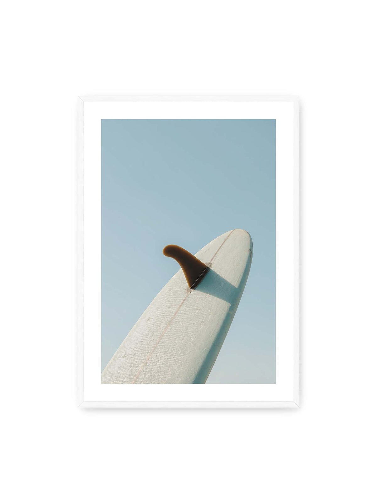 70x100 cm, weißer Galerie-Rand, weißer Rahmen – Helles Surfbrett mit dunkler Finne und markantem Schatten ragt diagonal vor einen klaren blauen Himmel.