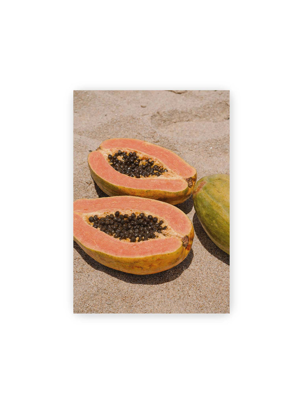 21x30 cm – Zwei geöffnete Papayahälften mit dunklen Samen und eine ganze Papaya auf hellem Sand.