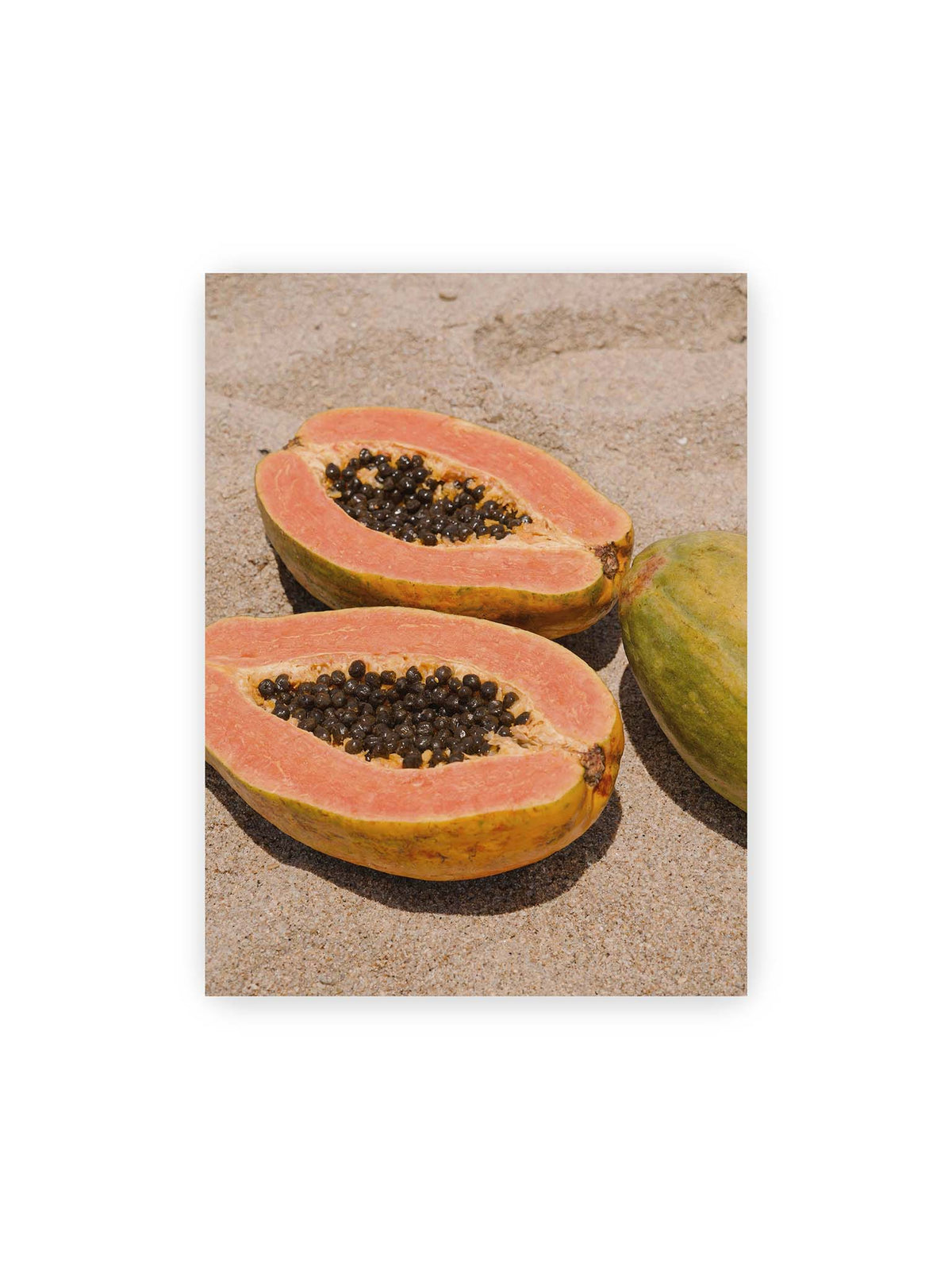 30x40 cm – Zwei geöffnete Papayahälften mit dunklen Samen und eine ganze Papaya auf hellem Sand.