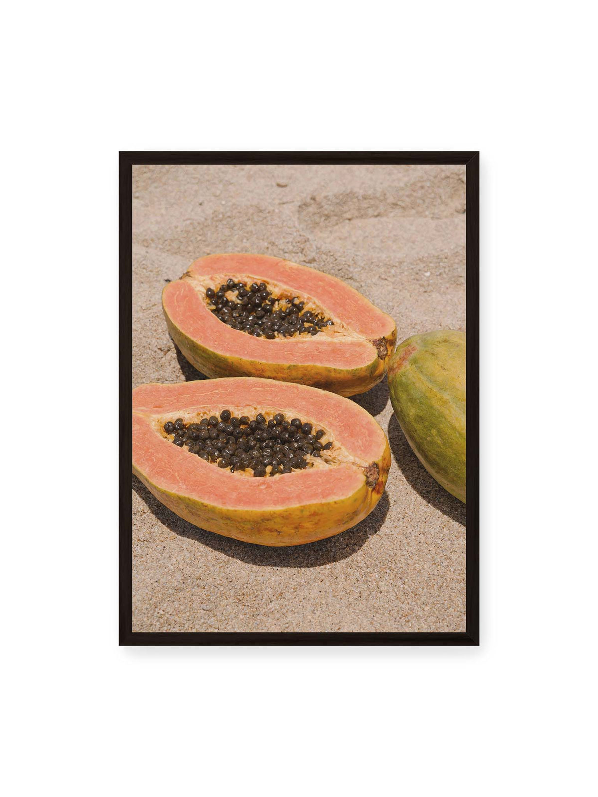 50x70 cm, schwarzer Rahmen – Zwei geöffnete Papayahälften mit dunklen Samen und eine ganze Papaya auf hellem Sand.