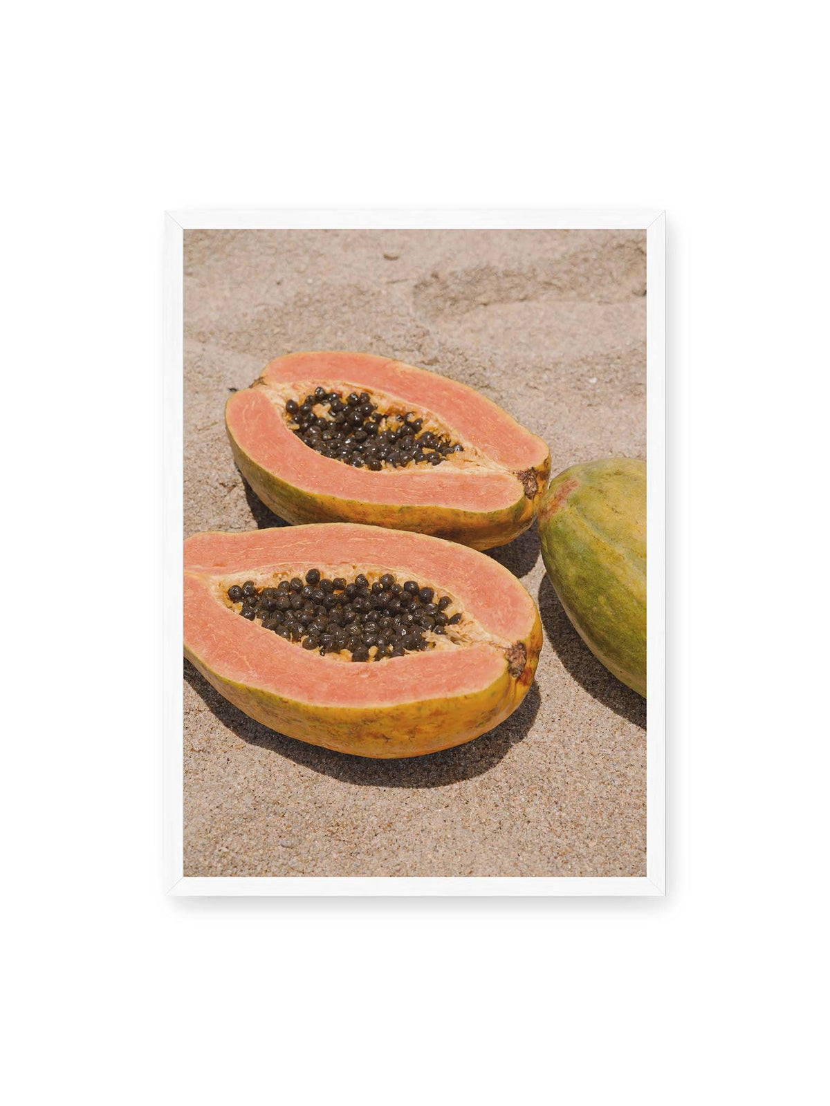 50x70 cm, weißer Rahmen – Zwei geöffnete Papayahälften mit dunklen Samen und eine ganze Papaya auf hellem Sand.