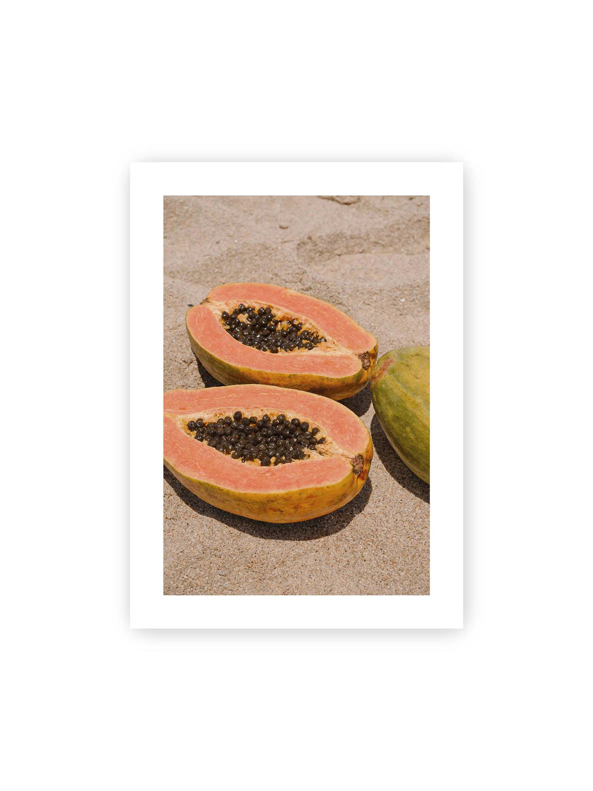 50x70 cm, weißer Galerie-Rand – Zwei geöffnete Papayahälften mit dunklen Samen und eine ganze Papaya auf hellem Sand.