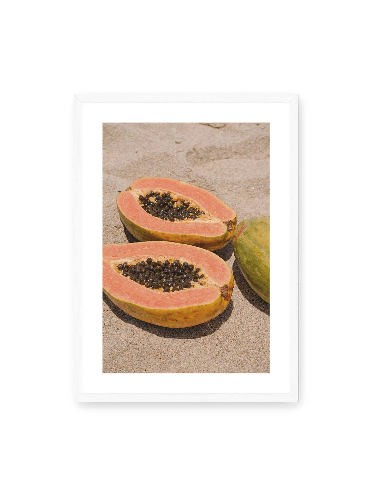 50x70 cm, weißer Galerie-Rand, weißer Rahmen – Zwei geöffnete Papayahälften mit dunklen Samen und eine ganze Papaya auf hellem Sand.