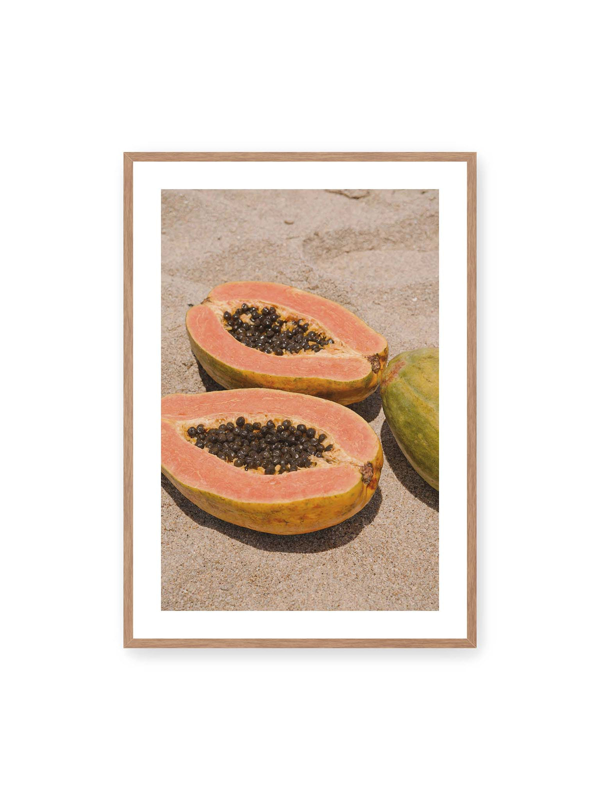 70x100 cm, weißer Galerie-Rand, Eichenrahmen – Zwei geöffnete Papayahälften mit dunklen Samen und eine ganze Papaya auf hellem Sand.