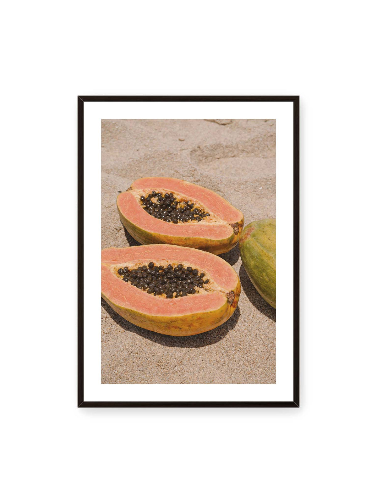 70x100 cm, weißer Galerie-Rand, schwarzer Rahmen – Zwei geöffnete Papayahälften mit dunklen Samen und eine ganze Papaya auf hellem Sand.